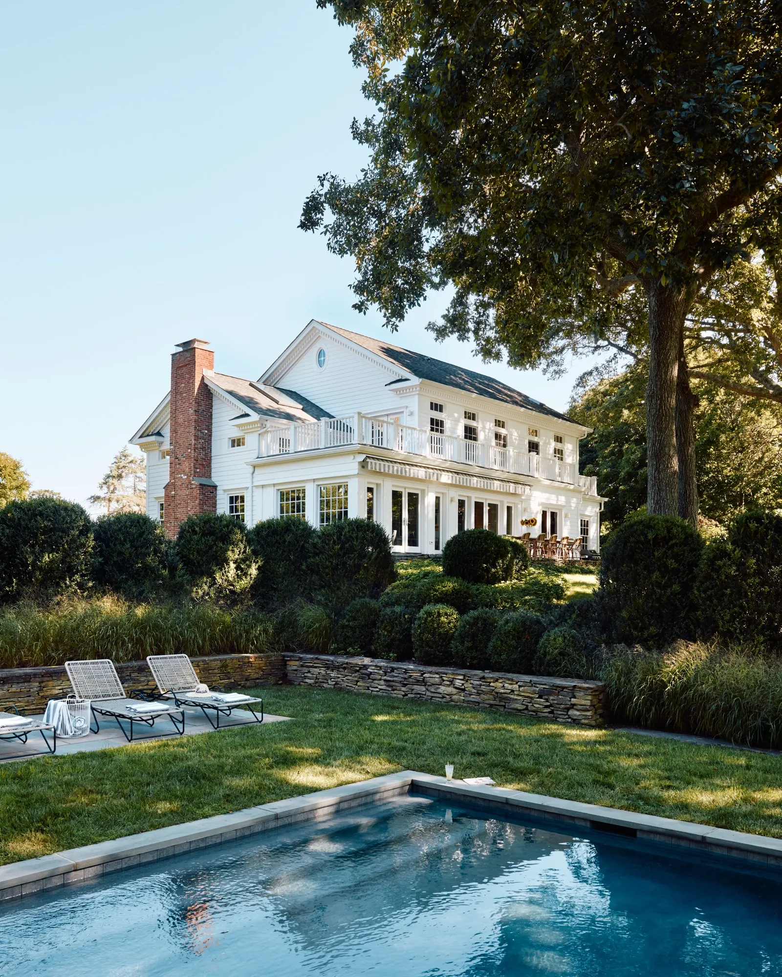 White colonial estate with pool and lounge chairs